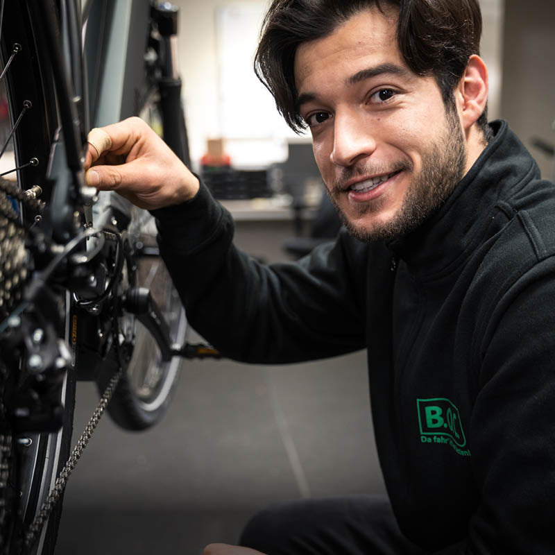 Ein Fachberater kniet neben einem Fahrrad in einer Werkstatt der Fahrrad-Filial-Kette B.O.C.