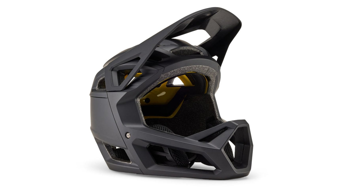 Der FOX Proframe MT BLK CE (MT BLK) ist ein mattschwarzer Enduro-Integralhelm mit kantigen Belüftungsöffnungen und einem Kinnschutz, der mit fortschrittlicher MIPS-Technologie ausgestattet ist und hier im Seitenprofil auf weißem Hintergrund abgebildet ist.